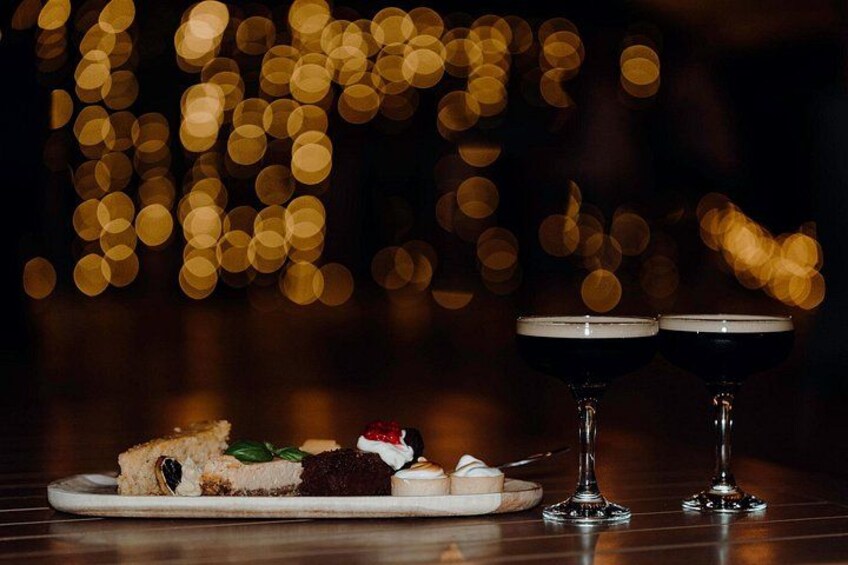 A dessert plate with cake and a glass of dark drink on a table with a blurred bokeh background. 5