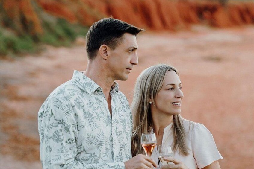 A man and a woman standing outdoors, holding glasses of a pink beverage. 2