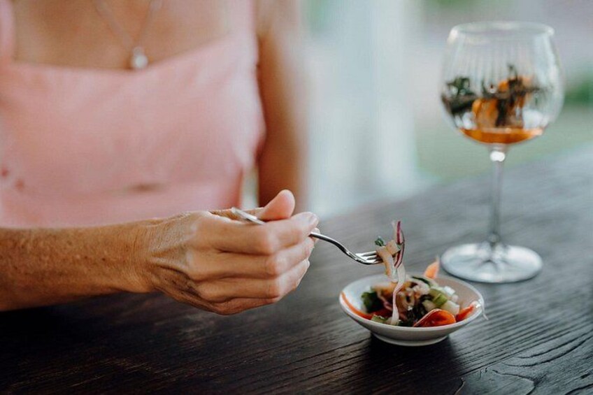 A person holding a fork with a salad, a wine glass, and a wooden table. 3