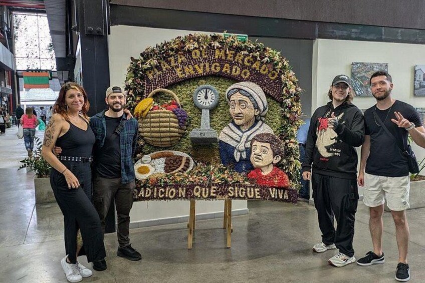A group of people standing in front of a decorative display with a clock and a sign that reads 'Tradicion Que Sigue Viva.' 4