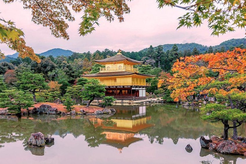 En traditionel japansk bygning afspejlet i en sø, omgivet af træer med efterårsfarver og en bjergkæde i baggrunden. 3