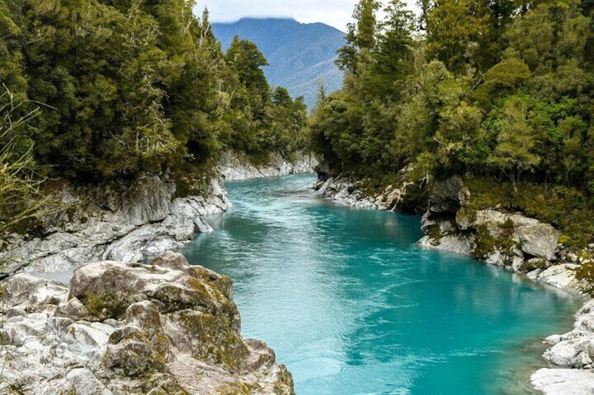 A turquoise river surrounded by rocky terrain and dense green forest. 1