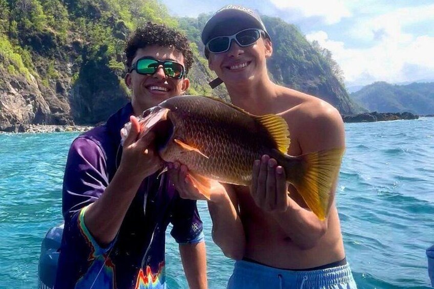 Two people holding a fish in a body of water with a mountainous landscape in the background. 4