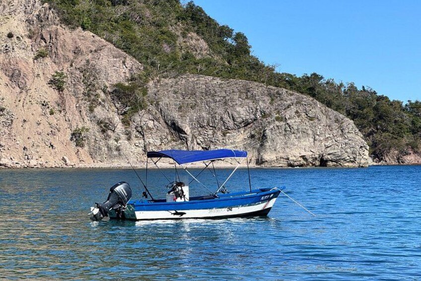A small blue boat with a canopy on a calm body of water, surrounded by rocky cliffs and greenery. 3