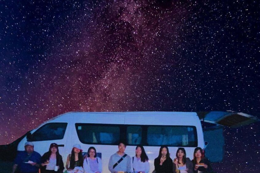 A group of people in front of a white van with a starry sky in the background. 2