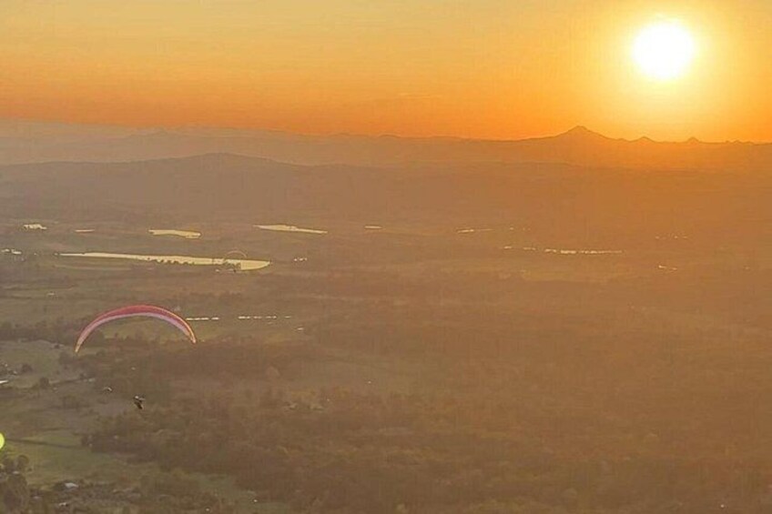 A landscape with a sun setting behind a mountain, a kite flying, and a body of water. 2