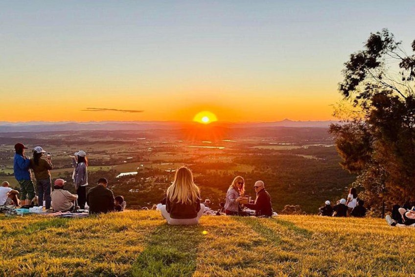 A sunset over a grassy hill with people sitting and standing, overlooking a valley. 4
