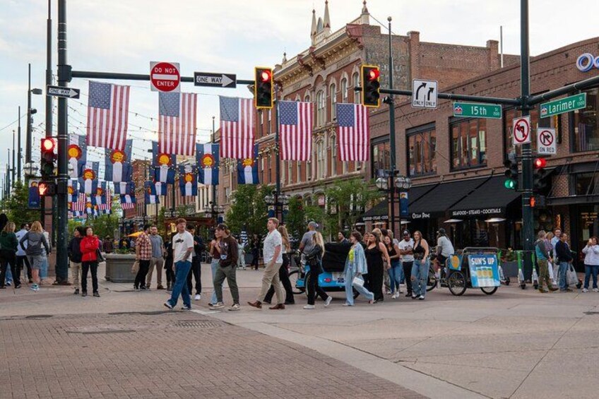 A busy intersection with pedestrians crossing, American flags, and historic buildings. 1