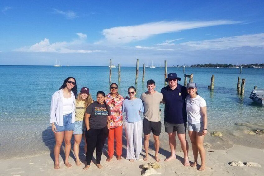 A group of people standing on a beach with clear blue water and wooden posts in the background. 3