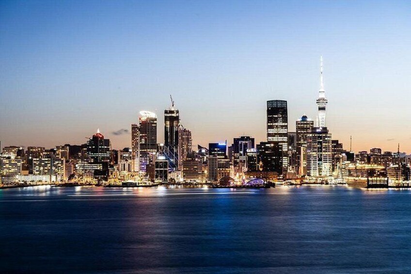 A city skyline at dusk with illuminated buildings and a prominent tower. 1