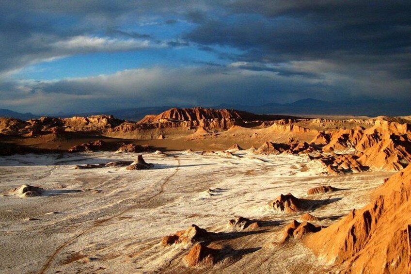 A desert landscape with rocky terrain and distant mountains under a cloudy sky. 4