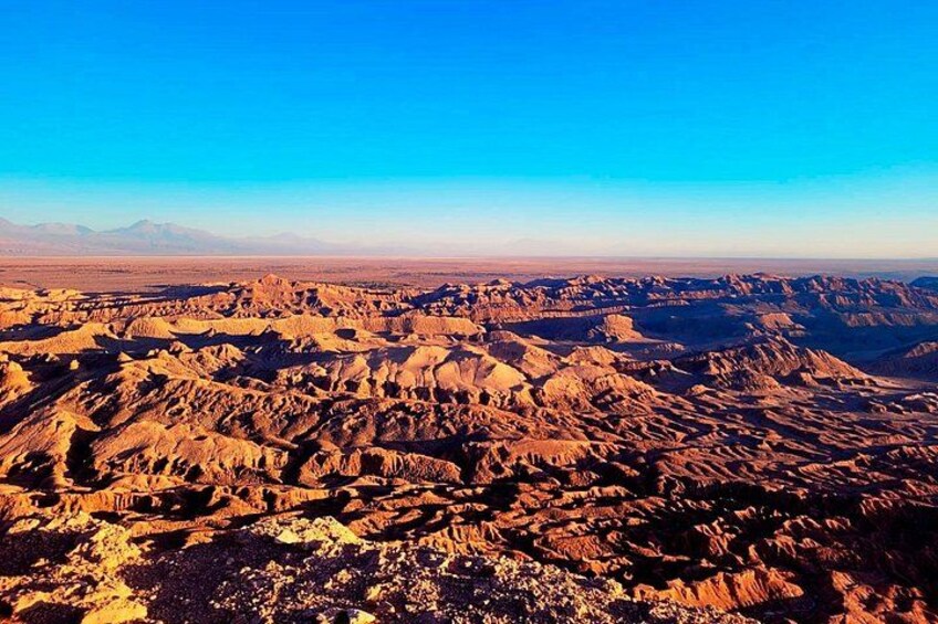 A vast desert landscape with rugged terrain and distant mountains under a clear blue sky. 5