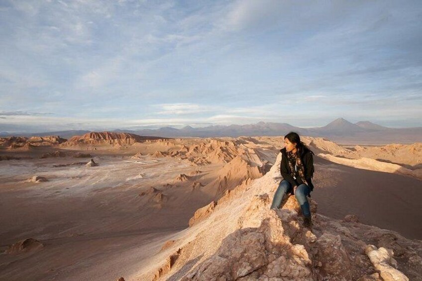 A person sitting on a rock formation in a desert landscape with mountains in the background. 2