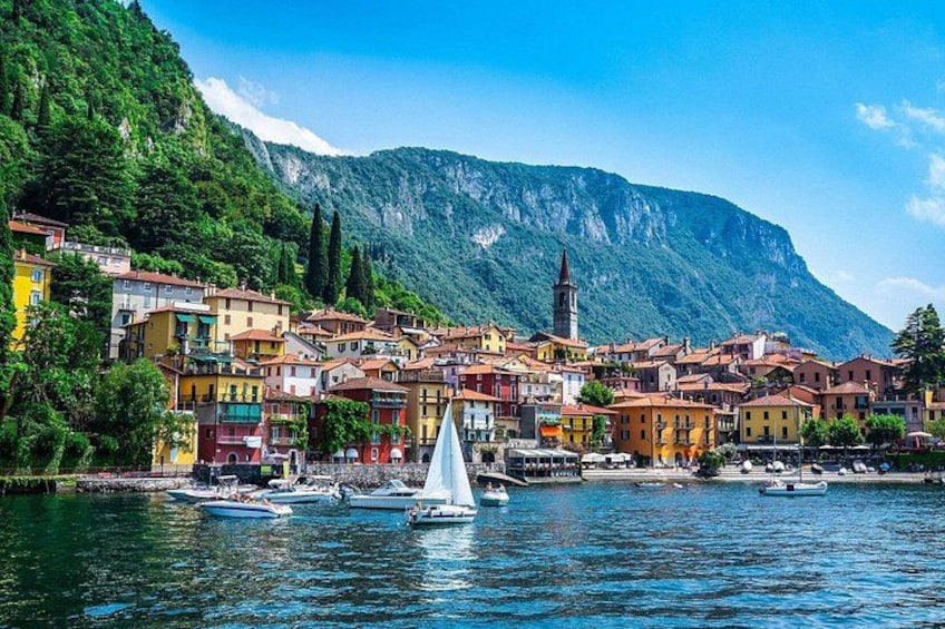 A coastal town with colorful buildings, a sailboat, and a mountain in the background. 1