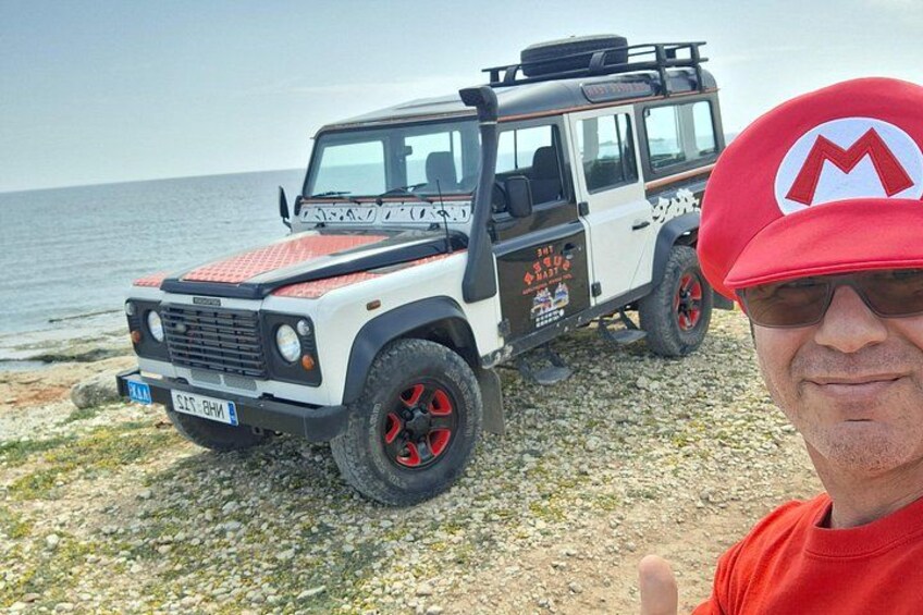 Un véhicule tout-terrain blanc, agrémenté de touches de rouge, est garé sur une plage rocheuse, avec l’océan en arrière-plan. 5