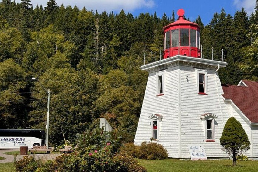 A white lighthouse with a red top, surrounded by greenery and a clear sky. 3