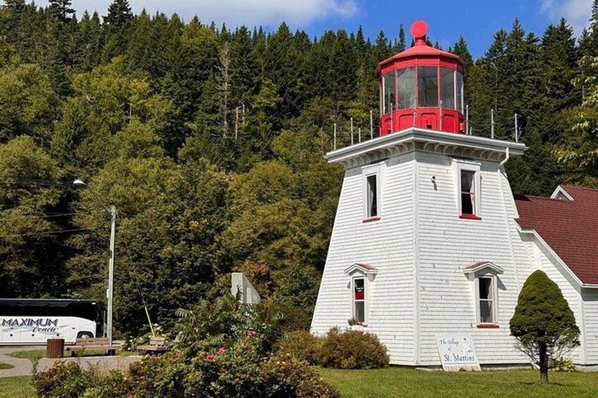A white lighthouse with a red top, surrounded by greenery and a clear sky. 5