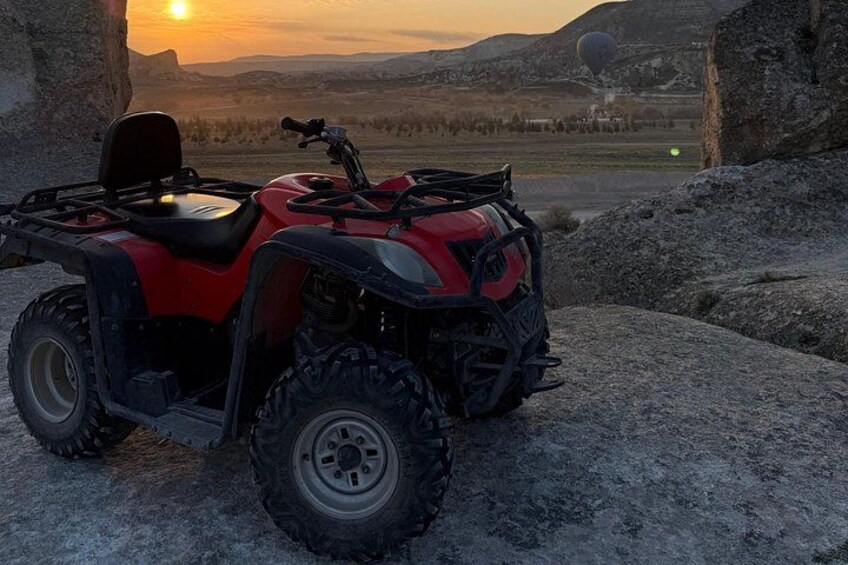A red ATV parked on a rocky surface with a sunset in the background. 4