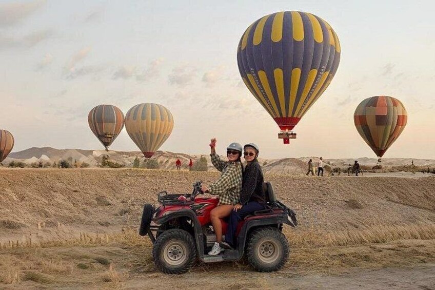 A desert landscape with multiple hot air balloons and a red ATV with two people. 1