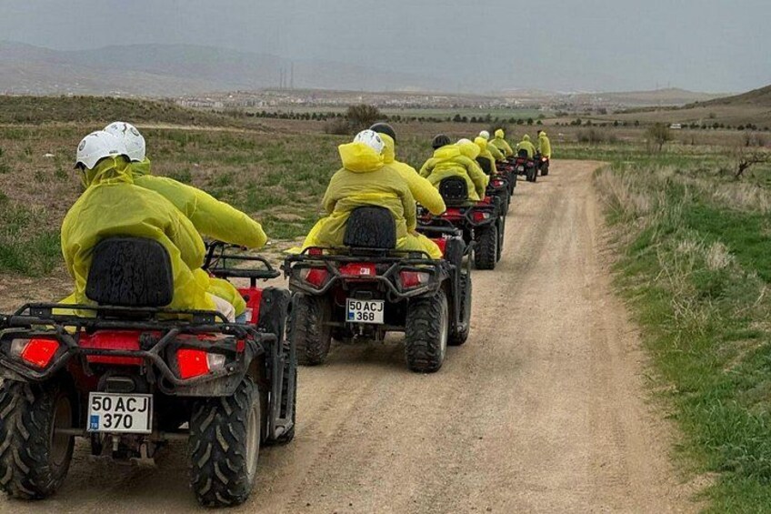 A group of people in yellow rain gear riding ATVs on a dirt road. 2
