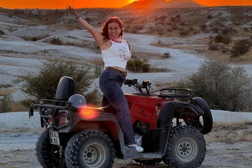 A person on a red ATV in a desert landscape with a sunset in the background. 5