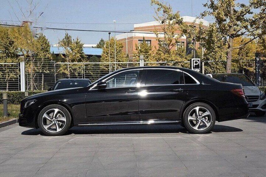 A black sedan parked in a lot with a parking sign and trees in the background. 4