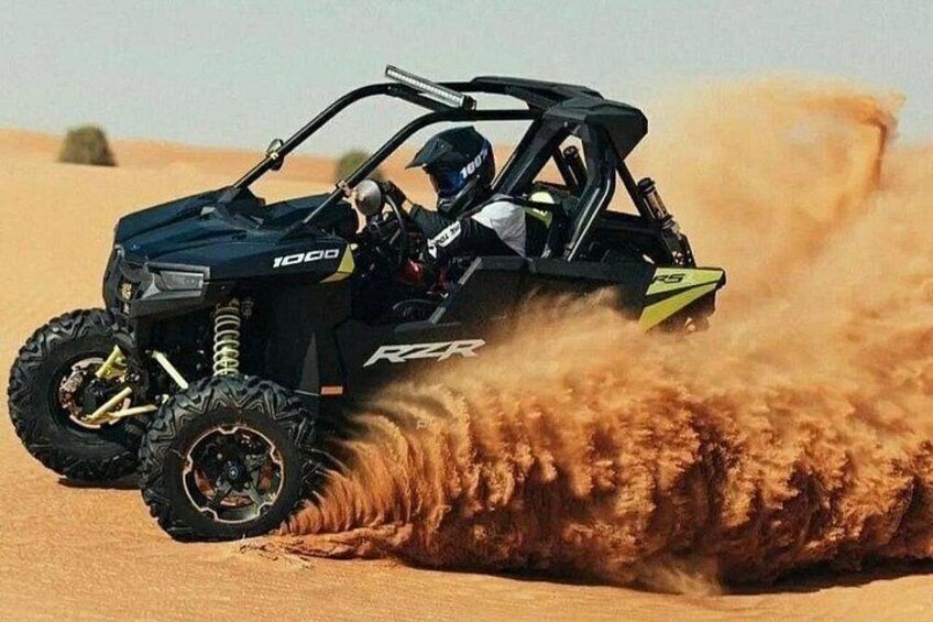 A black off-road vehicle with the number 1000 on the front, kicking up dust as it moves through a sandy terrain. 1