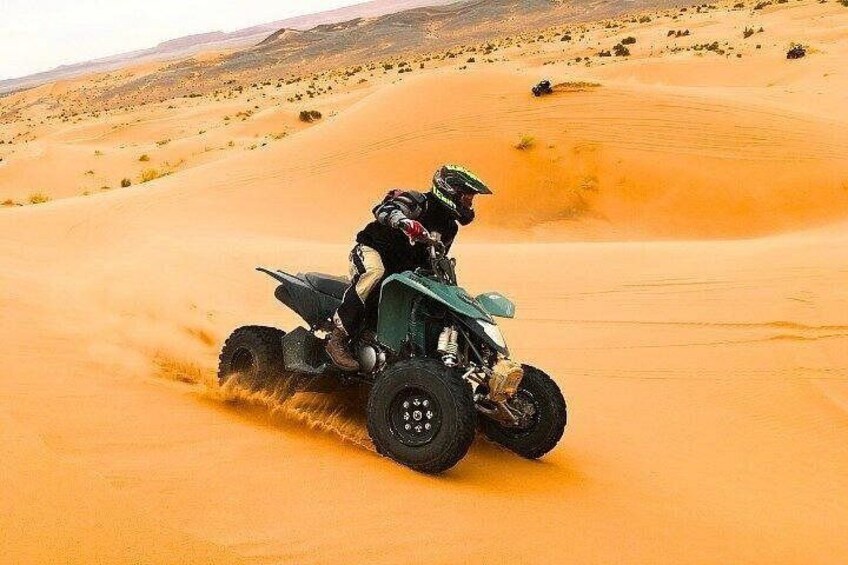 A person riding a quad bike on a sandy dune in a desert landscape. 2