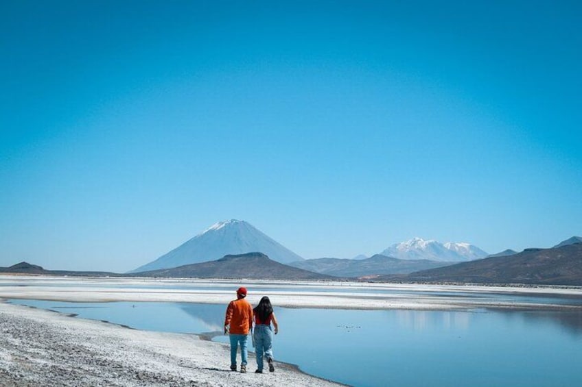 A couple walking along a frozen lake with mountains in the background. 3