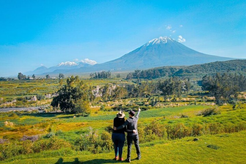 A couple standing on a grassy field with a mountain in the background. 2