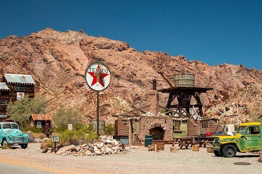 A vintage Texaco gas station with a red and white Texaco logo, a green vintage car, and a mountainous backdrop. 5