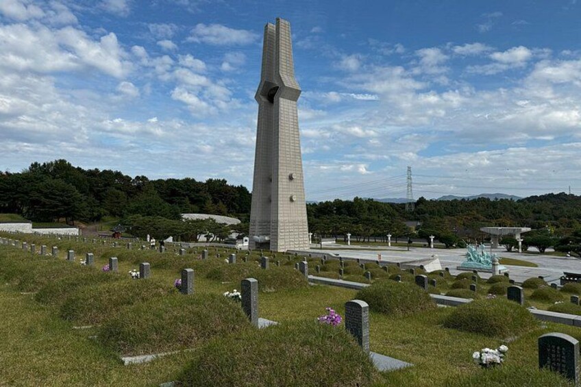 A tall monument in a cemetery with headstones and a statue in the background. 1