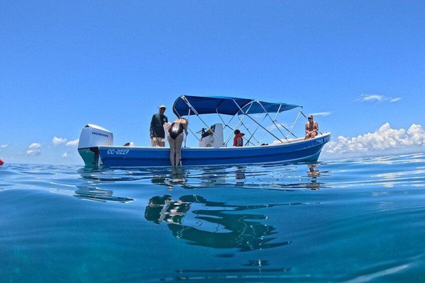 Ein blaues Boot mit Personen auf ruhigem, blauem Wasser unter einem wolkenlosen Himmel. 2