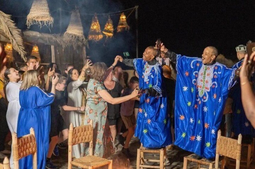 A group of people in a festive outdoor setting with traditional attire and a decorated stage. 4