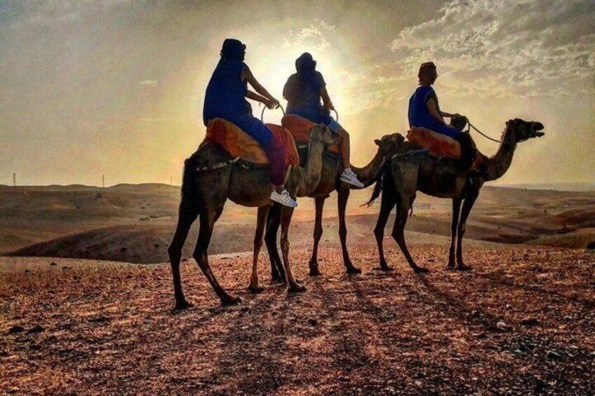 Three people riding camels in a desert landscape during sunset. 3