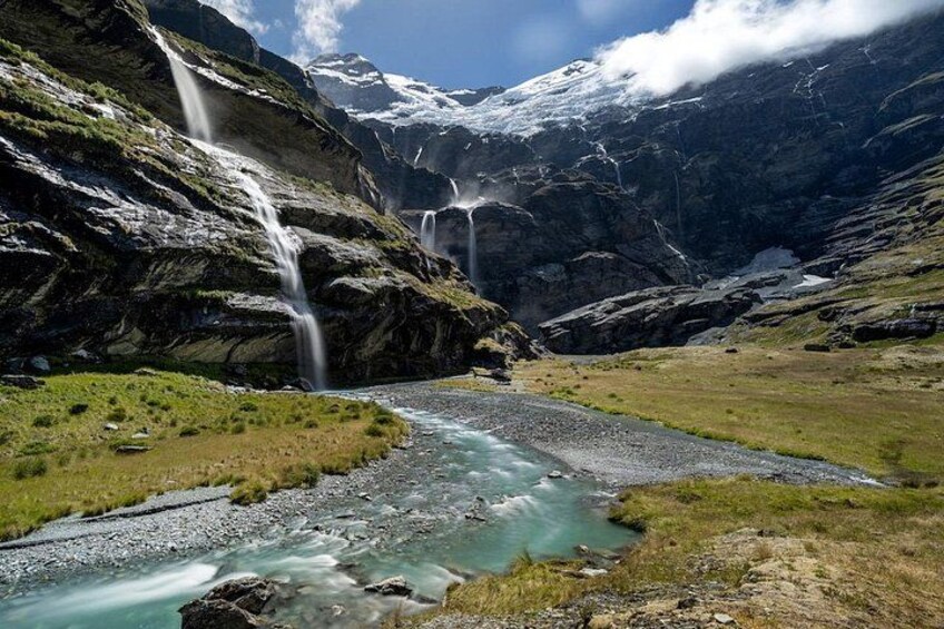A mountainous landscape with a river, waterfalls, and snow-capped peaks. 3