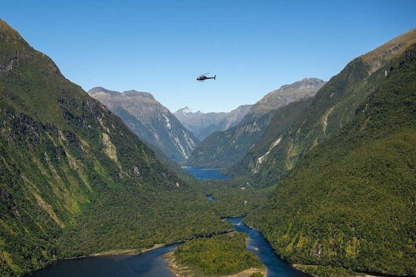 A helicopter flying over a valley with a river and mountains. 2