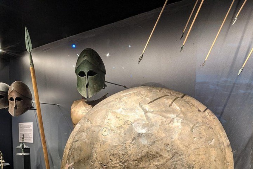 A museum display with ancient helmets, a spear, and a large spherical object. 5