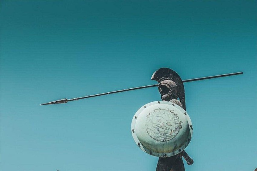 A bronze statue of a warrior with a spear and shield against a blue background. 2
