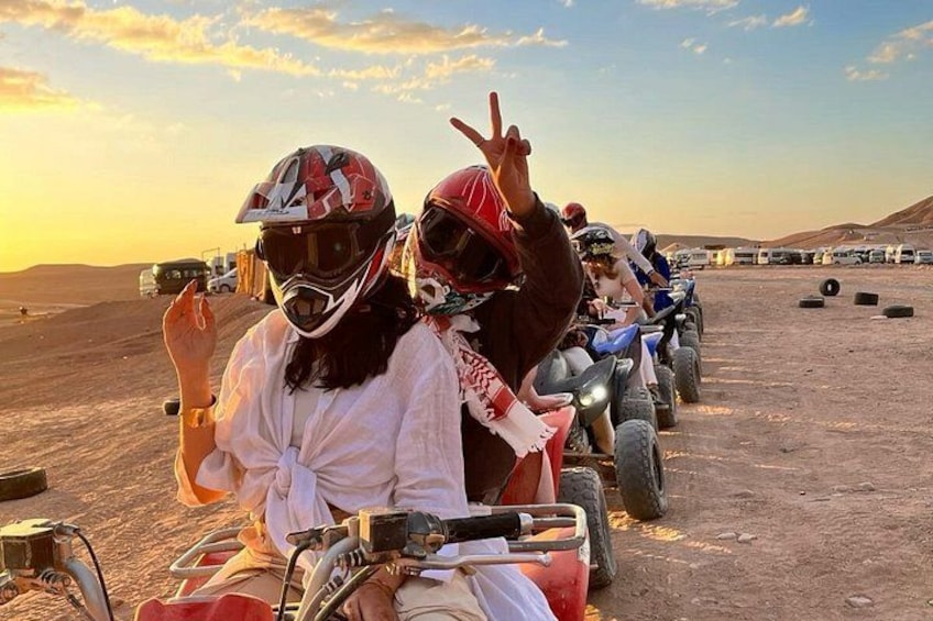 People on quad bikes in a desert setting with vehicles and hills in the background. 1