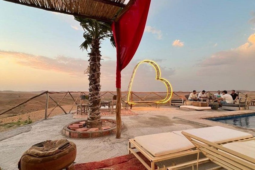 A desert landscape with a pool, lounge chairs, and a group of people sitting around a table. 1