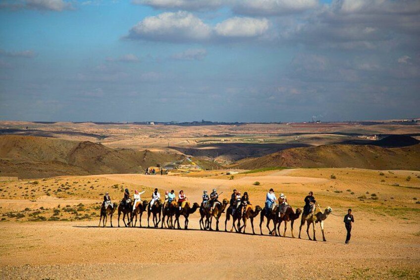 A group of people on horseback and camels in a desert landscape with rolling hills and a distant city skyline. 5
