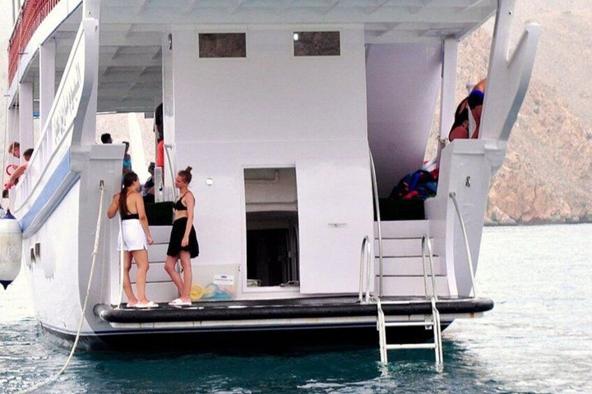 A boat with a ladder leading to a platform, people on the deck, and water in the background. 5