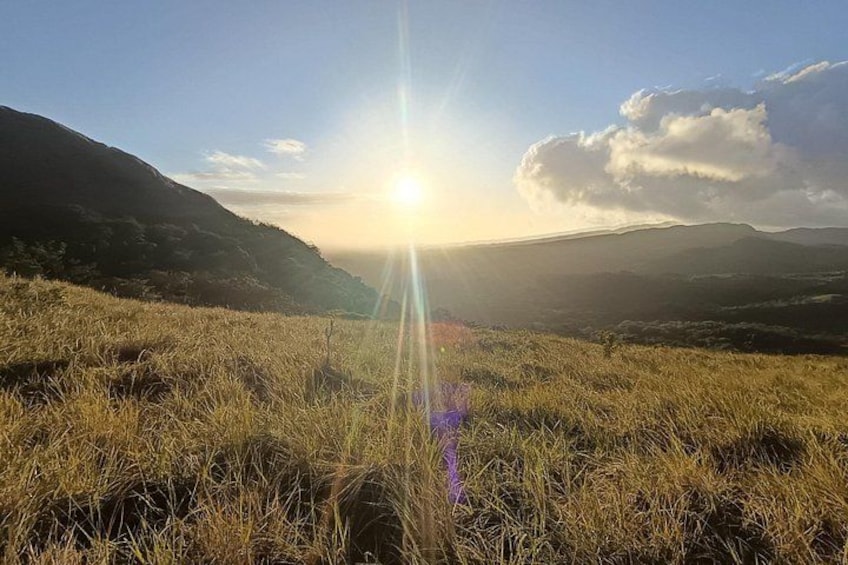 A grassy field with a mountain in the background and the sun low on the horizon. 3