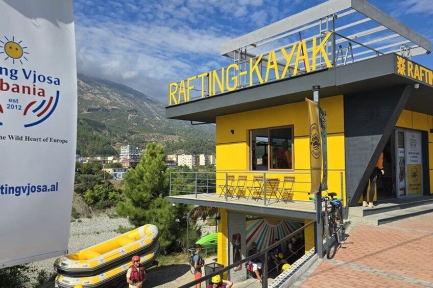 A yellow building with 'RAFTING KAYAK' signage, a mountain in the background, and a sign for 'Rafting Viosa Albania' on the left. 2