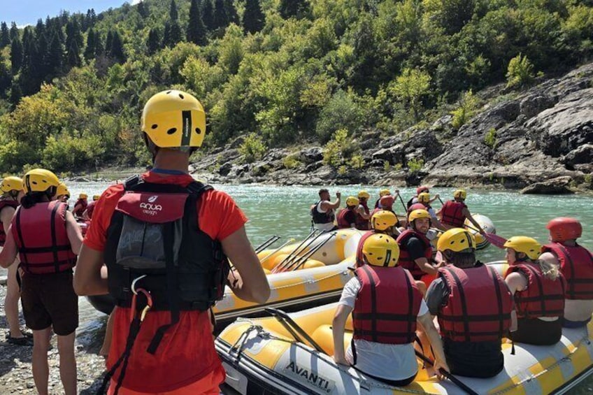 A group of people in a yellow inflatable raft on a river, wearing helmets and life jackets. 5