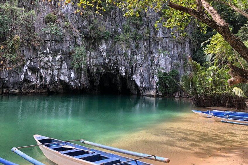 A calm river with clear water, boats, and a rocky cliff with vegetation. 2