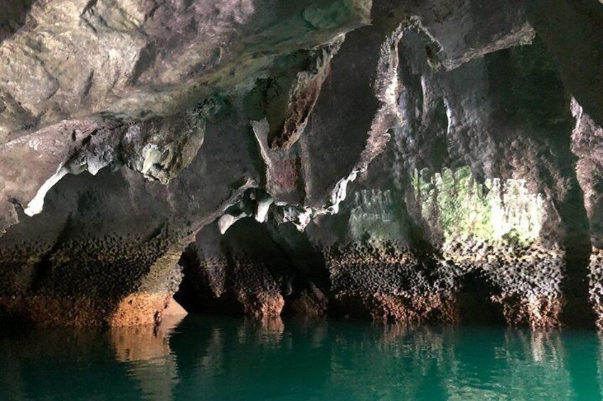 Interior de una cueva con estalactitas y estalagmitas, agua reflejando la luz y una poza en el fondo. 2