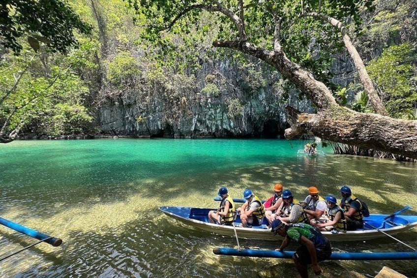 Un grupo de personas en un bote en un río turquesa y cristalino, rodeado de vegetación exuberante y acantilados rocosos. 5