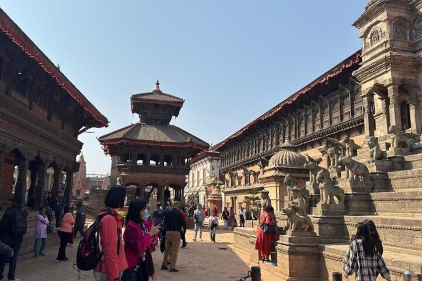 A historical building with a central pagoda-like structure, surrounded by stone statues and visitors. 3
